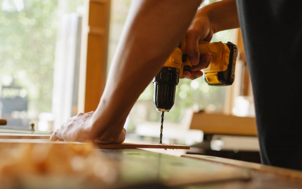 Close-up of a person using a power drill on wood indoors during daytime.