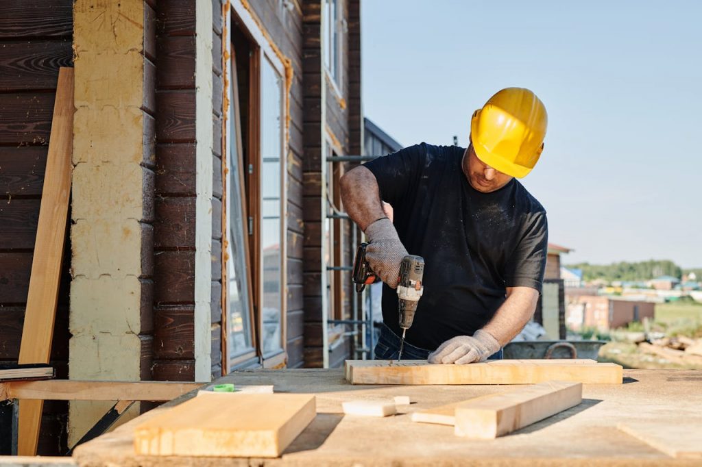 A construction worker using a power drill on a building site, outdoors during the day.